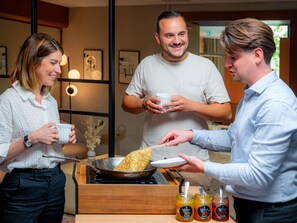 Une personne sert une crêpe dans une poêle à deux personnes qui tiennent des tasses.
