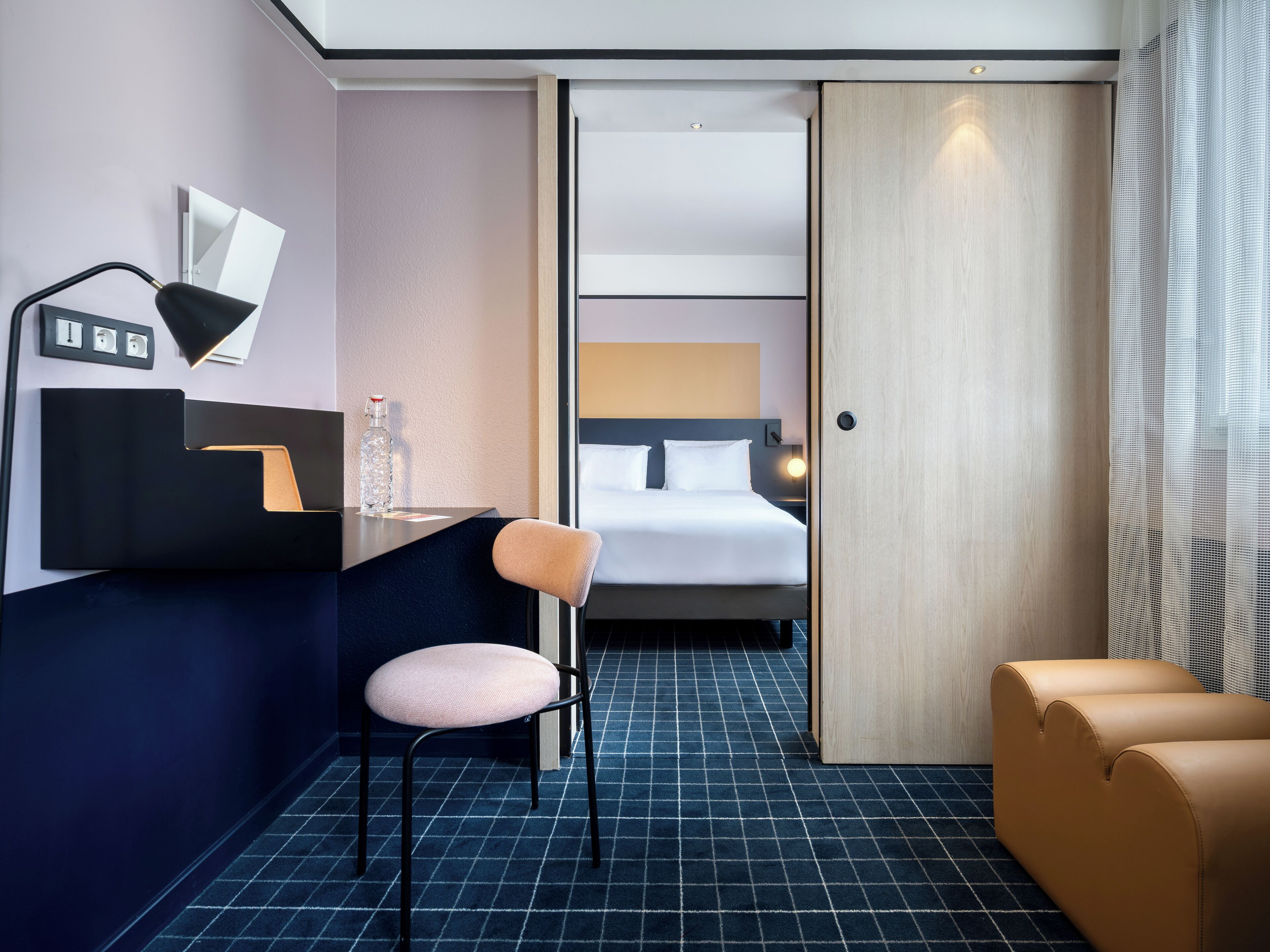 Habitación de hotel con escritorio, silla, cama y vista a través de una puerta.