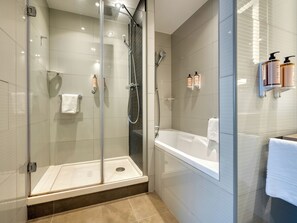 Un baño moderno con ducha de vidrio, una bañera independiente y un tocador con artículos de aseo.