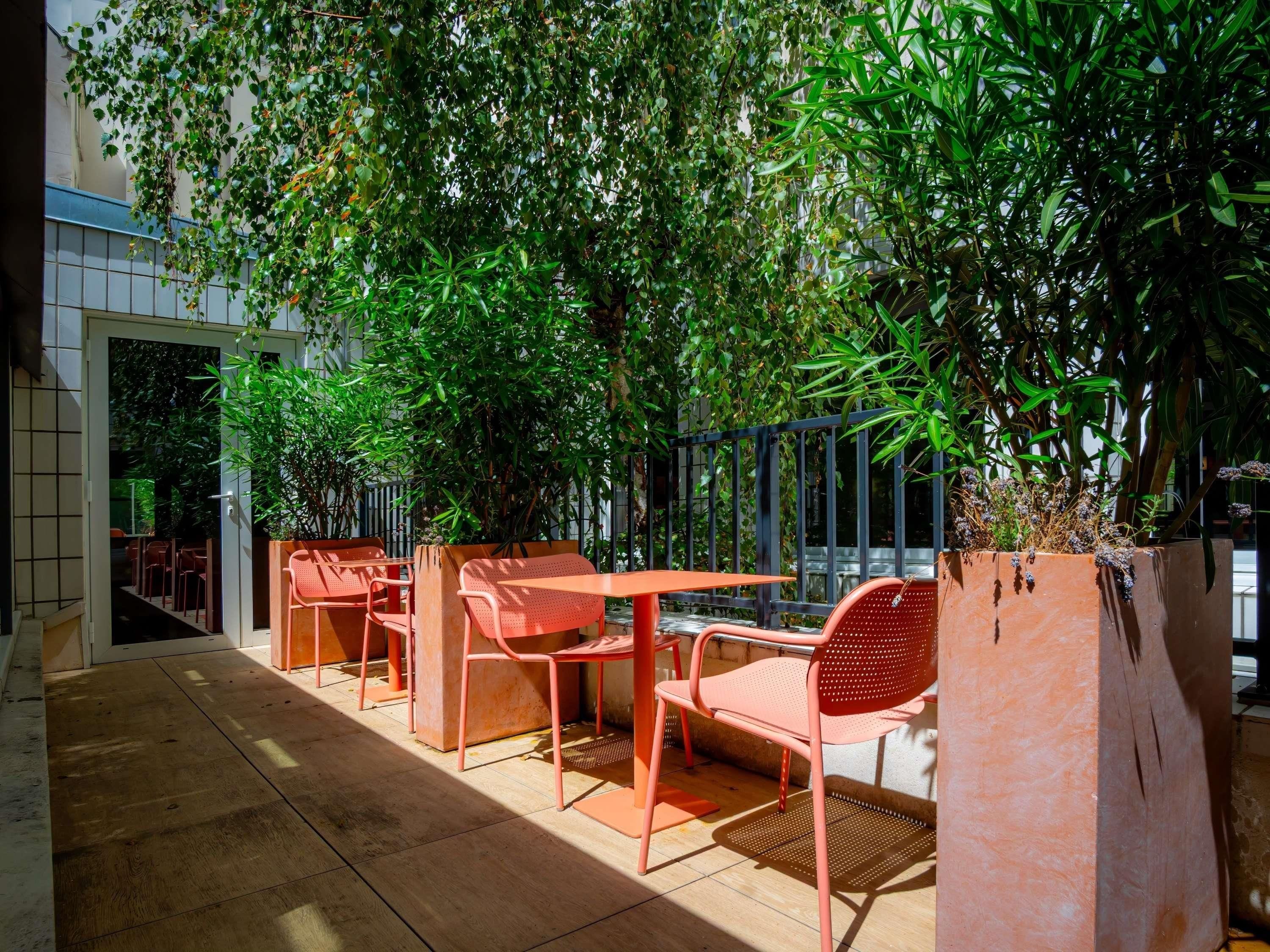 An outdoor seating area with tables and chairs, surrounded by lush greenery and a tiled floor.