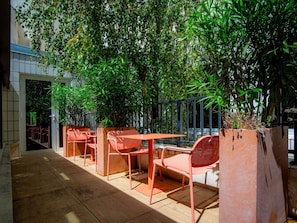 Un espace extérieur aménagé avec des tables et des chaises, entouré d’une végétation luxuriante et doté d’un sol carrelé.