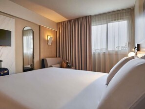 Una habitación de hotel con una cama grande, un escritorio, una silla, un espejo, una ventana con cortinas y una televisión.