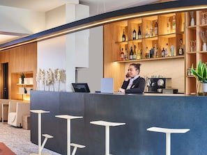Uma área de bar moderna com uma prateleira de madeira exibindo diversos frascos, um laptop no balcão e uma máquina de café.