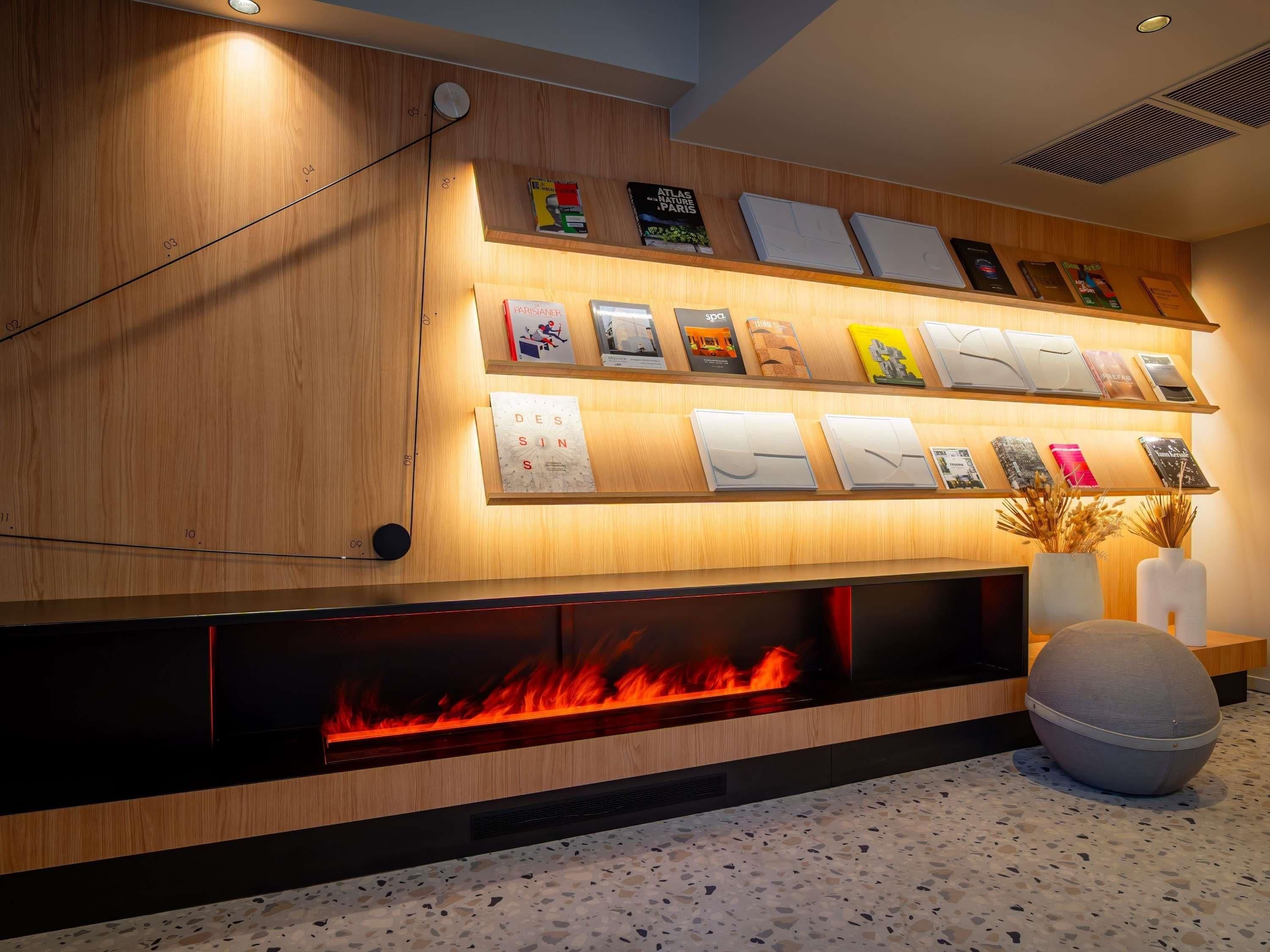 A modern interior with a wooden wall, a fireplace with visible flames, and a series of framed items on shelves.