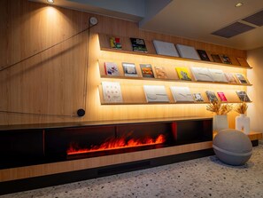 Un intérieur moderne avec un mur en bois, une cheminée dont on peut voir les flammes et une série d’objets encadrés disposés sur des étagères.