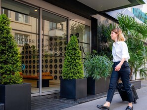 L’entrée d’un hôtel avec une façade en verre, un mur décoré d’une horloge et des plantes en pot.