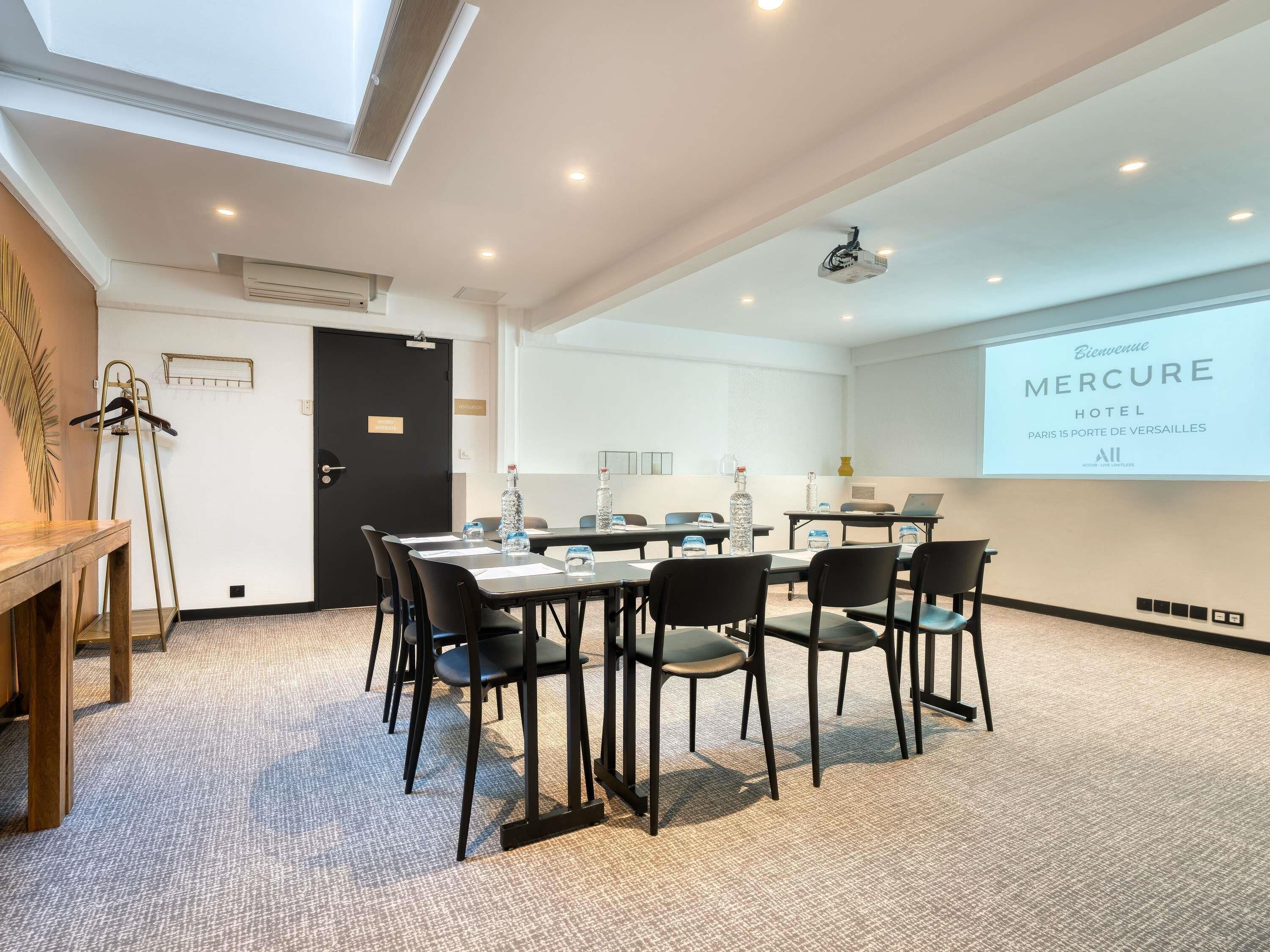 A conference room with a long table, chairs, a projector screen, and a door with a sign.