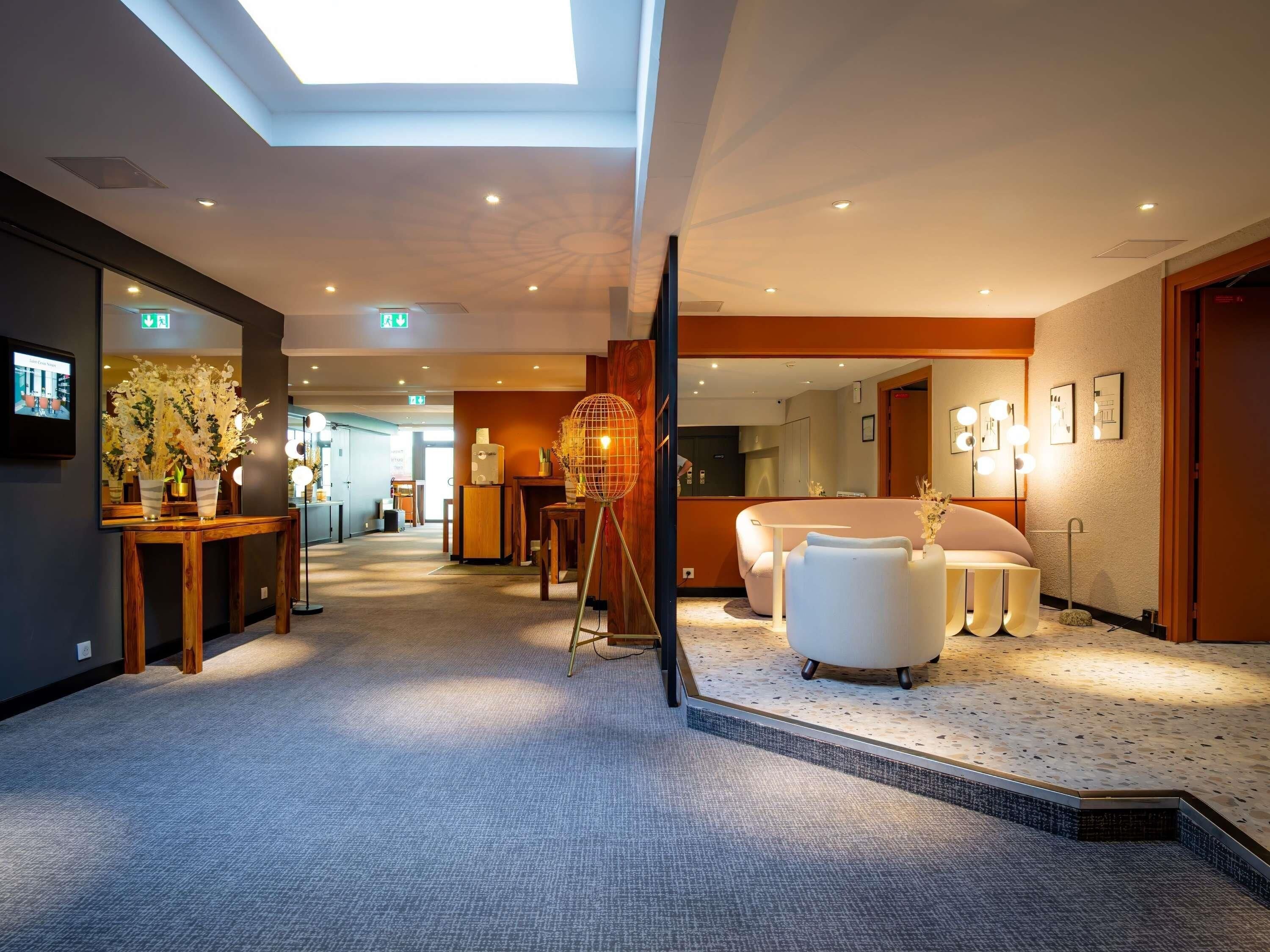 A hotel lobby with a reception desk, seating area, and a large mirror reflecting the space.