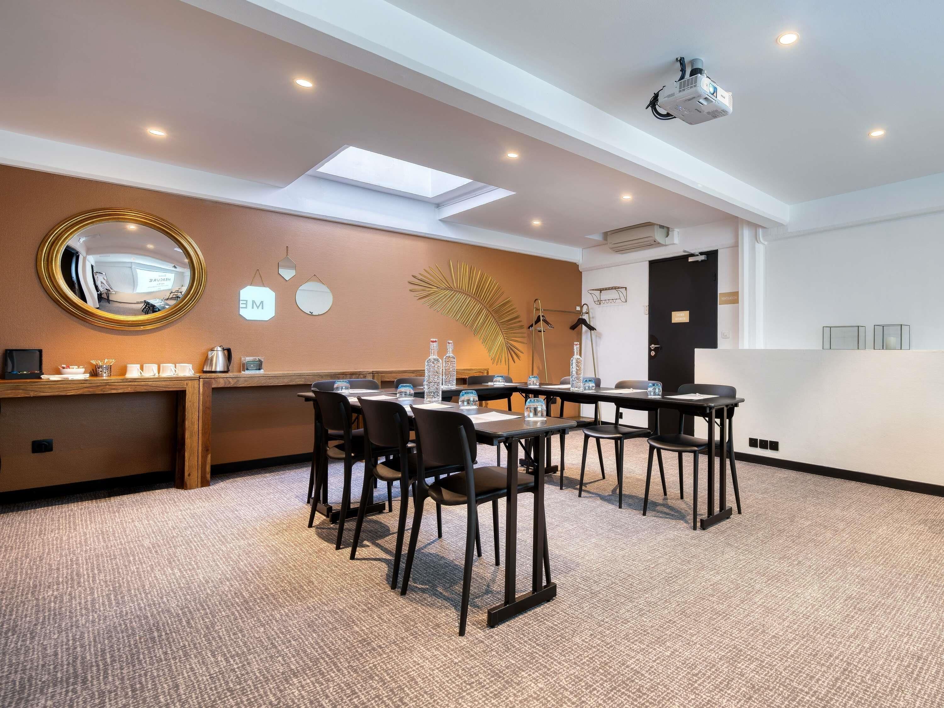 A conference room with a long table, chairs, a projector, and a mirror on the wall.
