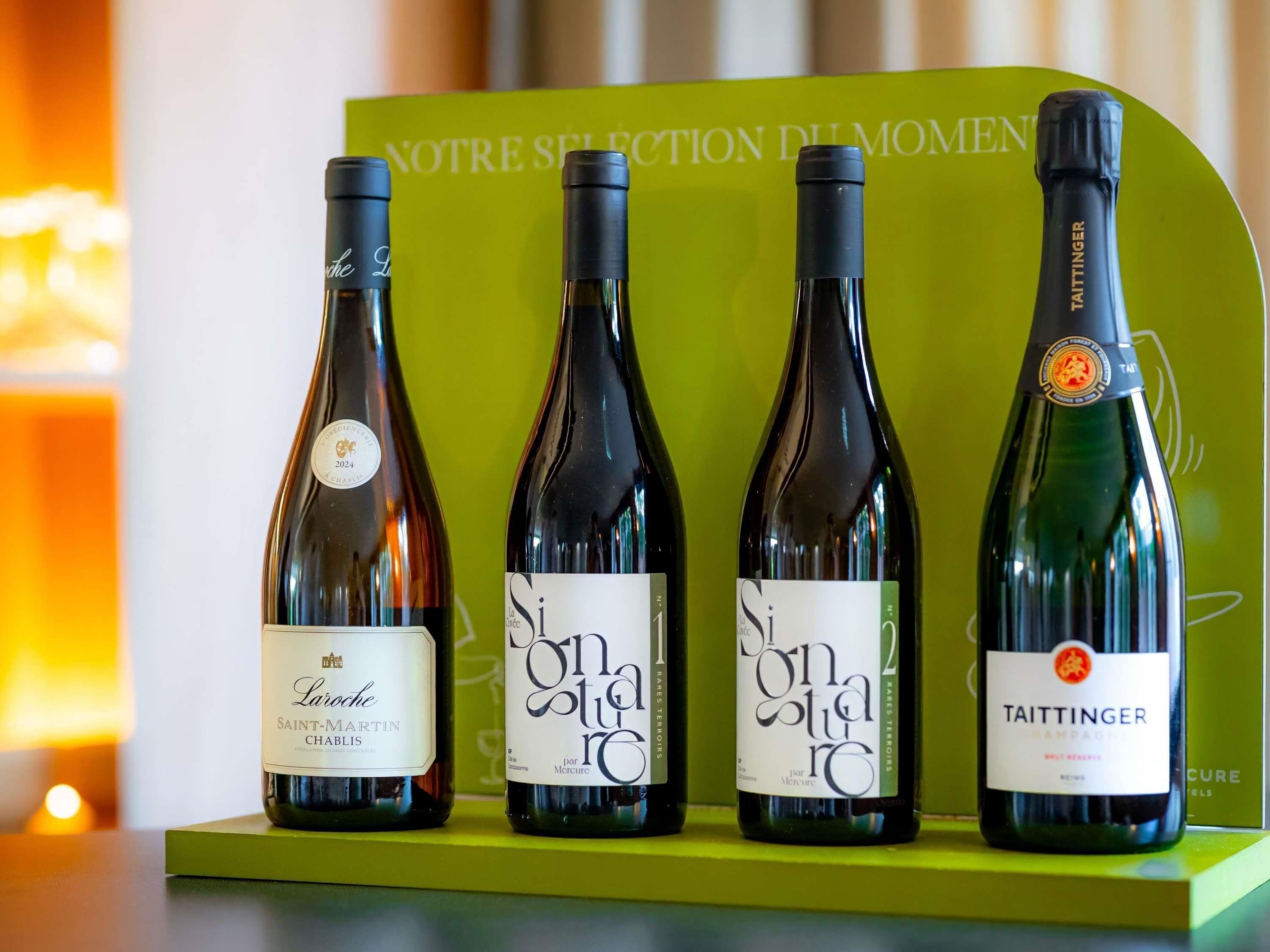 Cuatro botellas de vino sobre un pedestal verde, con un fondo que dice 'NOTRE SELECTION DU MOMEN'.