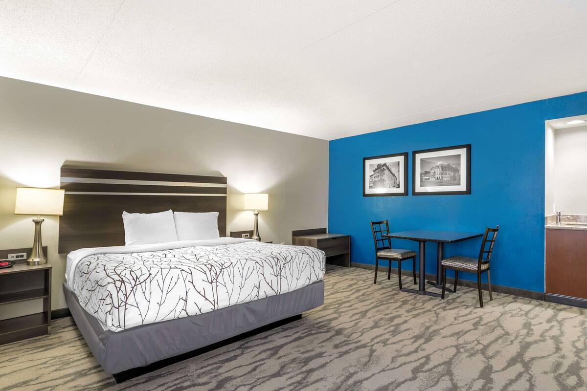 Une chambre d’hôtel comprenant un lit, des tables de chevet, un bureau avec des chaises et deux tableaux encadrés accrochés au mur.