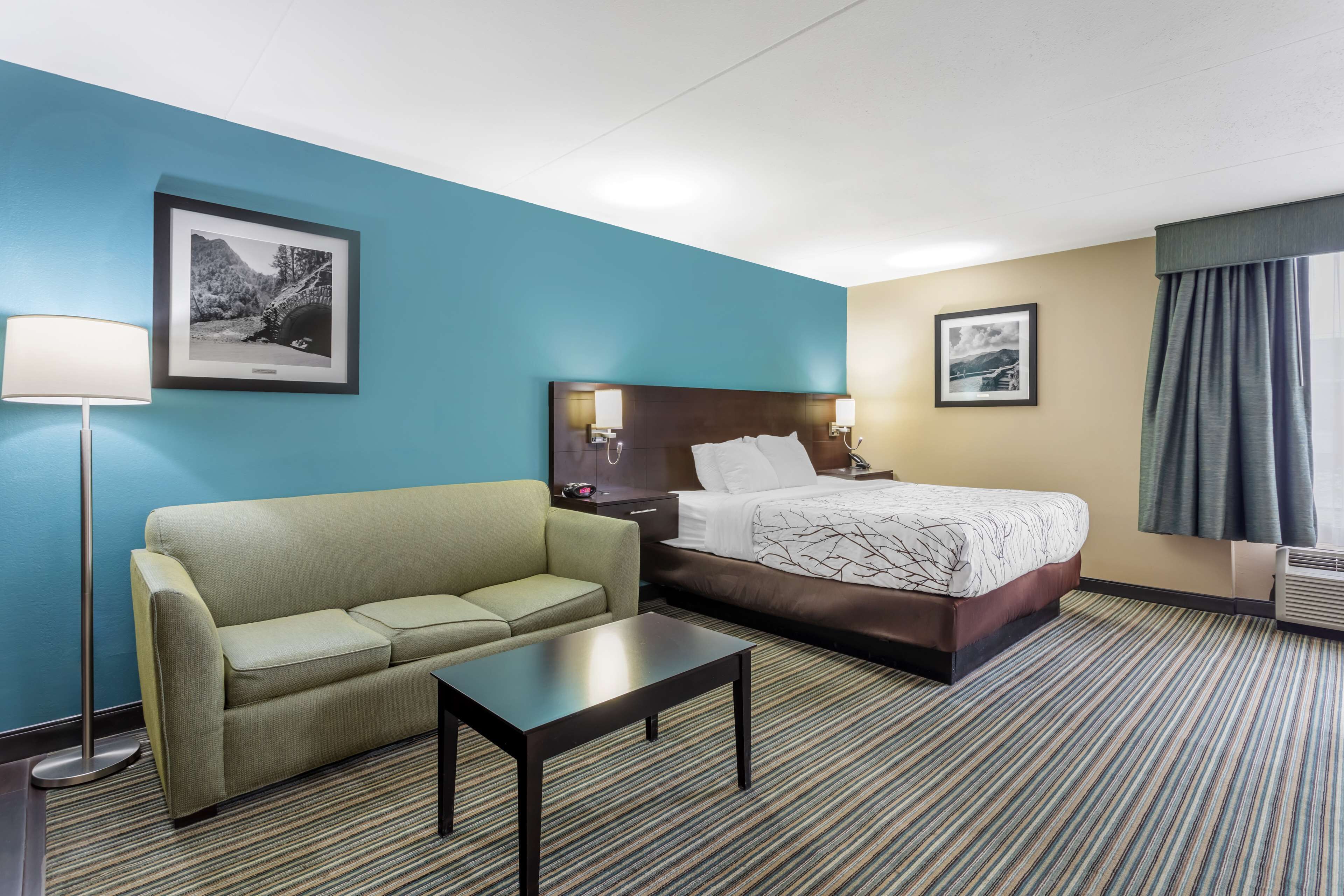 A hotel room with a bed, a sofa, a small table, and two wall-mounted lamps.