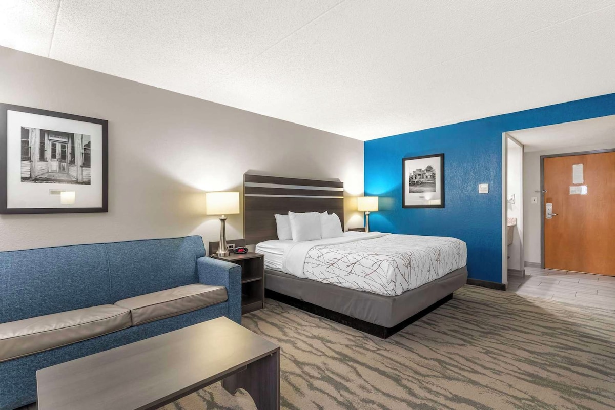 Une chambre d’hôtel avec un lit, un canapé bleu, une petite table et deux lampes fixées au mur.