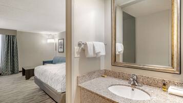 A hotel room with a bed, a bathroom with a granite countertop sink, and a large mirror.