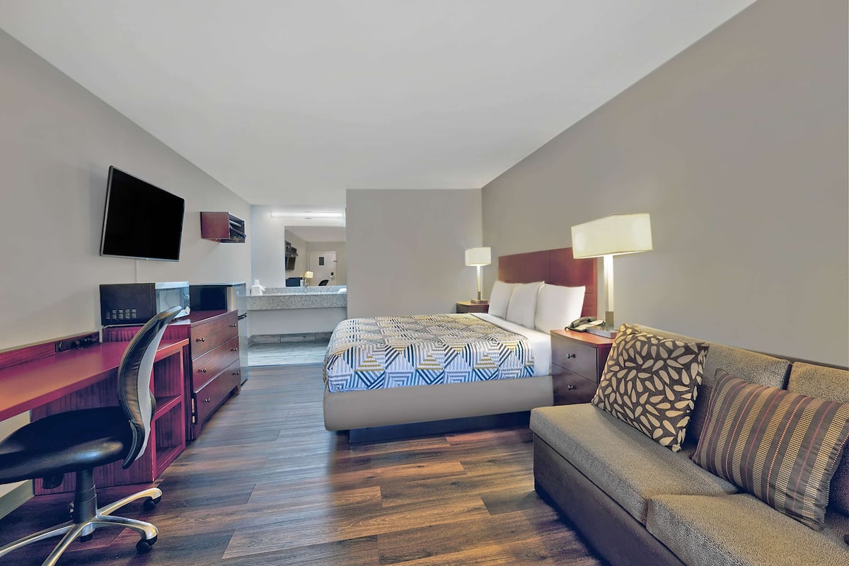 Ein Hotelzimmer mit einem Bett, einem Schreibtisch, einem Sessel, einem Fernseher, einer Lampe und einem Sofa.