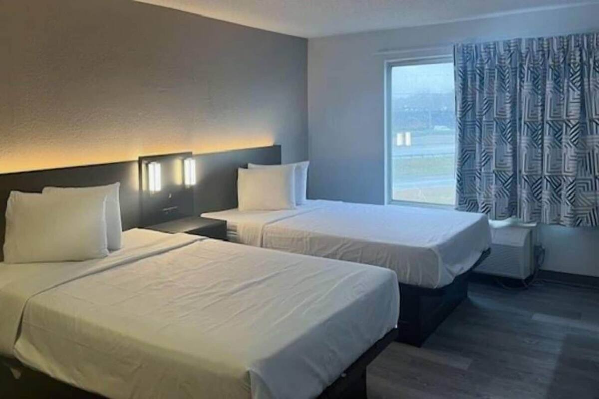 A hotel room with two beds, a large window with patterned curtains, and a nightstand between the beds.