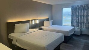 A hotel room with two beds, a large window with patterned curtains, and a nightstand between the beds.