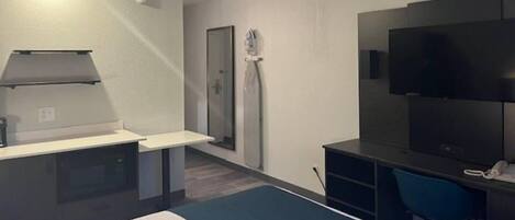 A hotel room with a bed, a desk with a chair, a flat-screen TV, and a shower area.