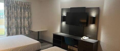 Habitación de hotel con dos camas, un escritorio, una silla, un televisor montado en la pared y un teléfono.