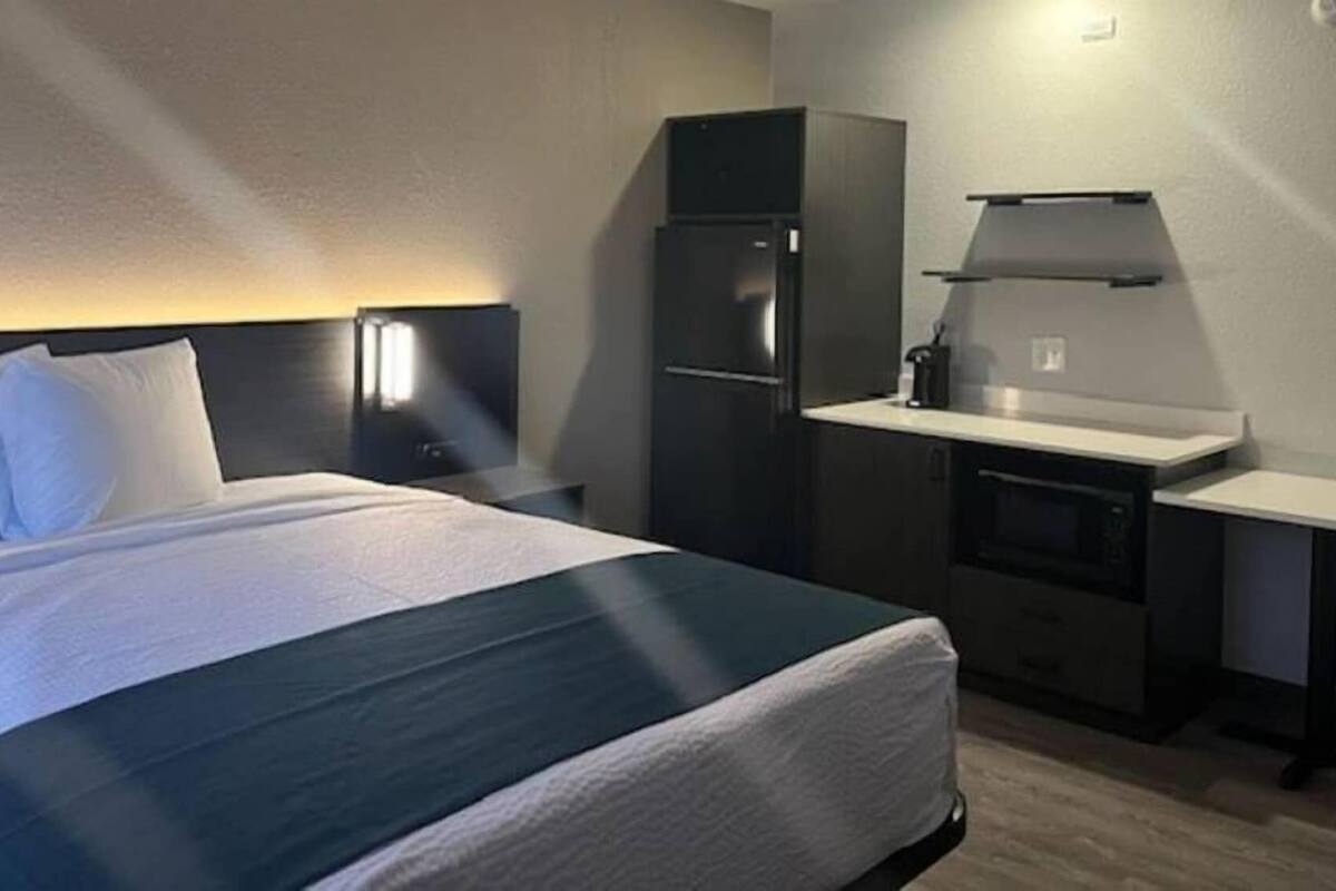 A hotel room with a bed, a small kitchenette, and a nightstand.