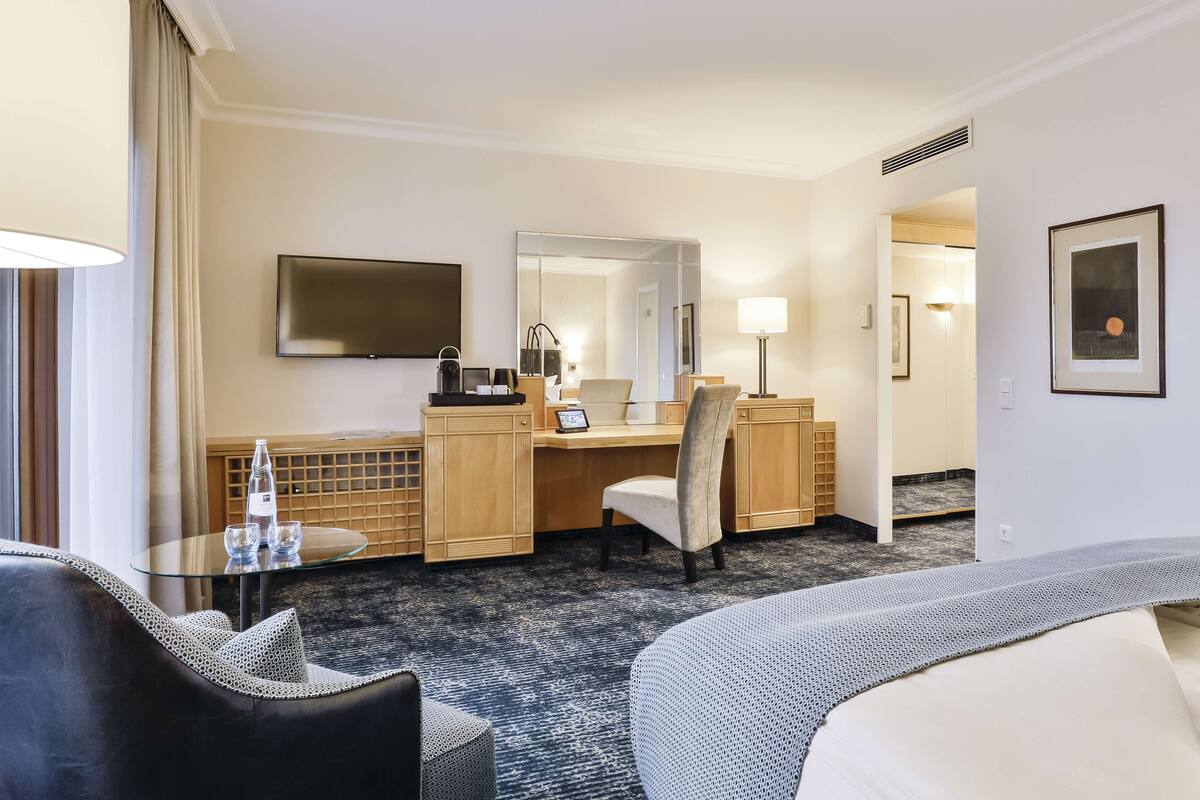 A hotel room with a bed, a desk, a chair, a TV, a mirror, and a window with curtains.
