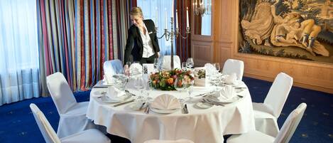 Un comedor formal con una mesa redonda dispuesta para una comida, rodeada de sillas blancas, y un gran mural en la pared.