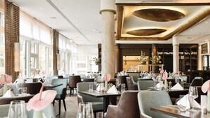A restaurant with multiple tables set for dining, featuring a modern interior with large windows and a bar area in the background. - Dorint Venusberg Bonn (Bonn)