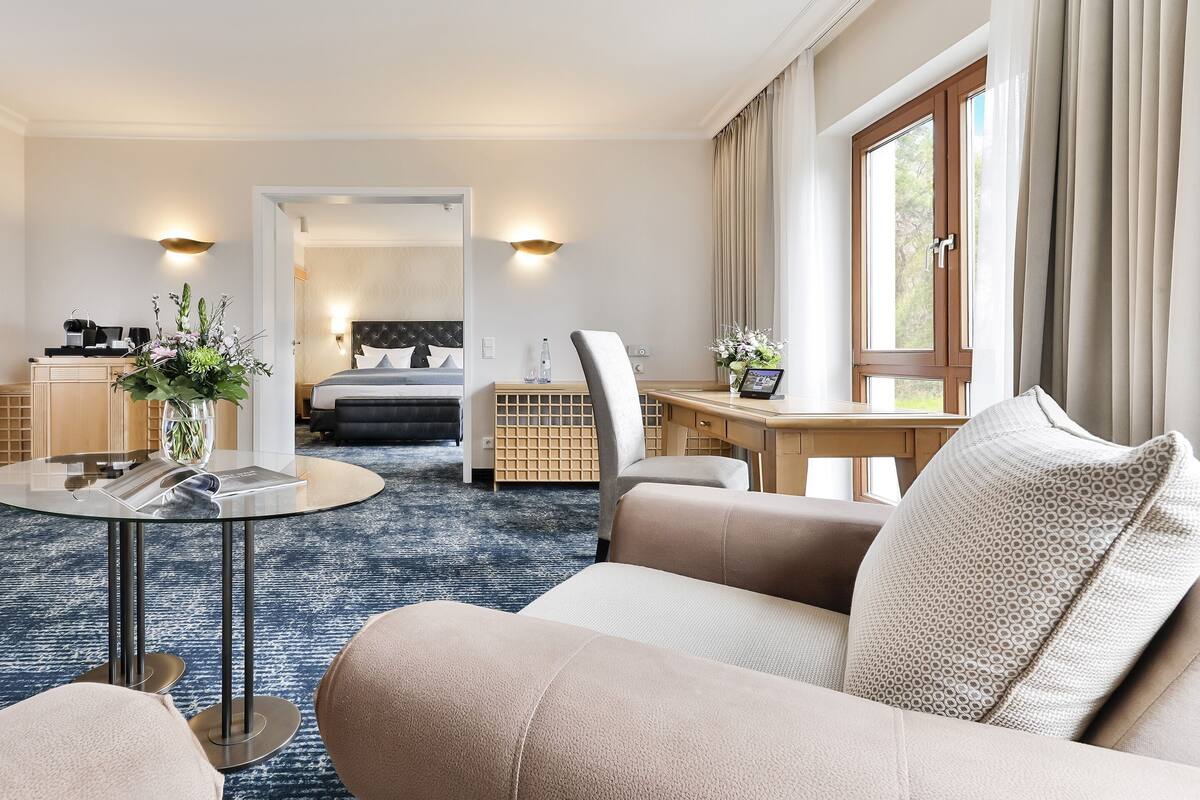 A hotel room with a bed, a sitting area with a coffee table, a desk, and a large window.
