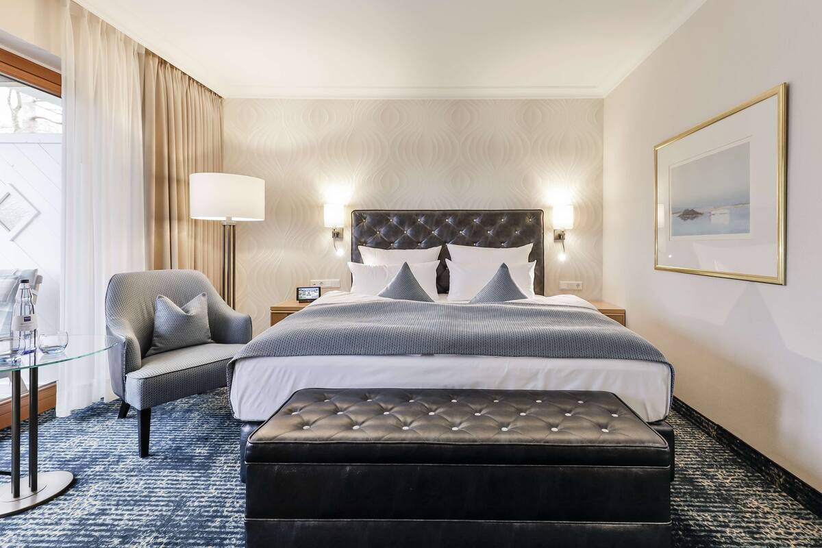 A hotel room with a bed, a chair, a table, and a lamp.