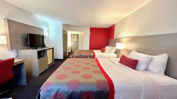 Habitación de hotel con una cama, un escritorio, un televisor y una puerta que da a otra habitación.