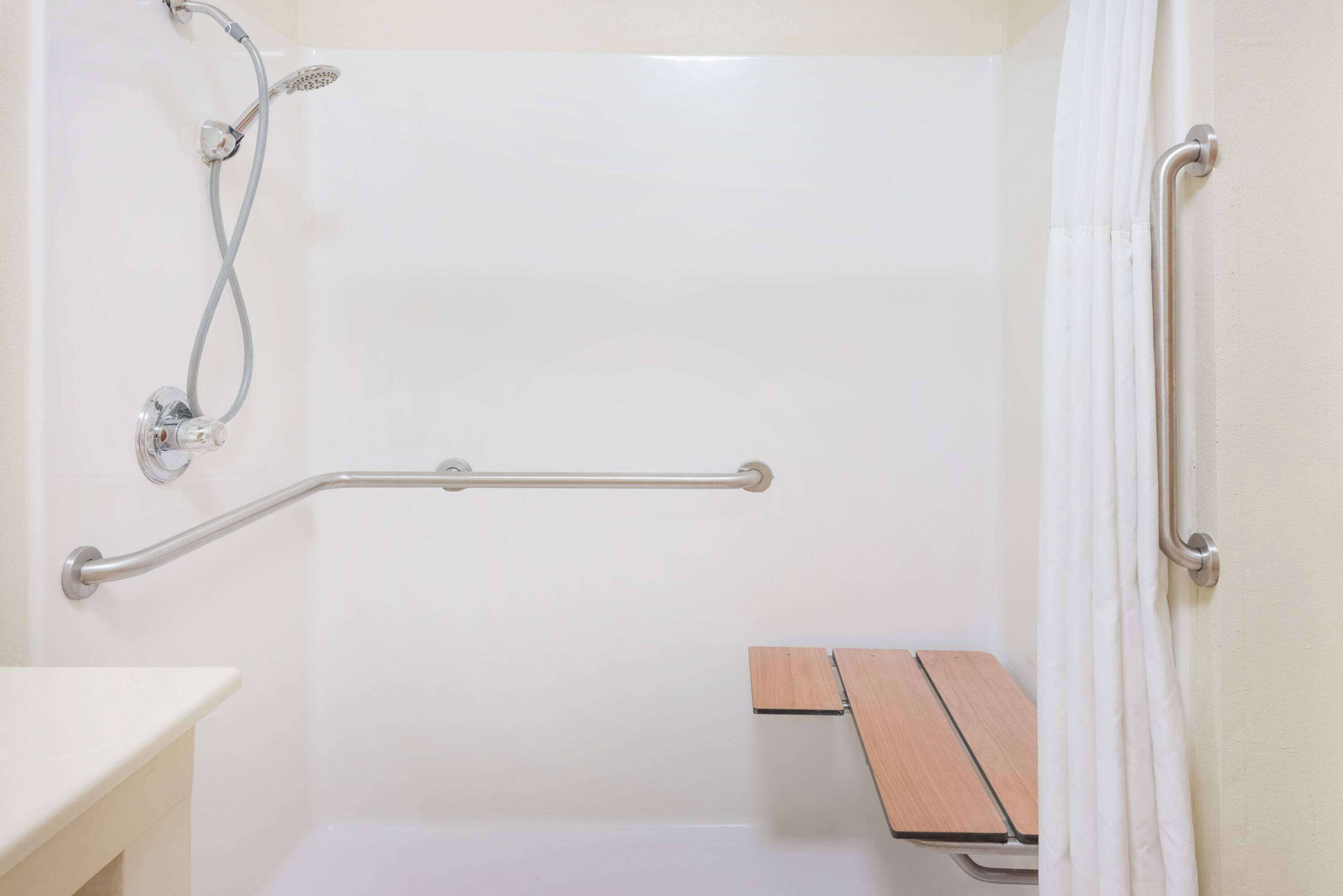Un baño con ducha, barras de apoyo y un banco.
