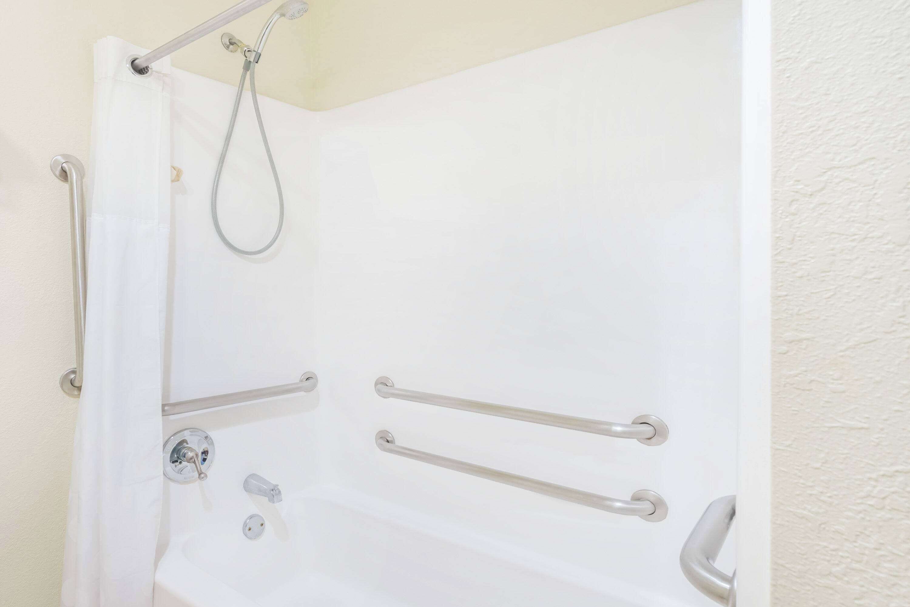 Une baignoire blanche équipée de barres d’appui, d’un pommeau de douche et d’un robinet.