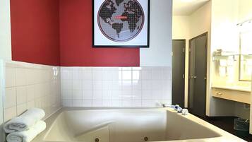 Een badkamer met een groot bad, witte tegels, een rode accentmuur en een wereldkaart in een lijst.