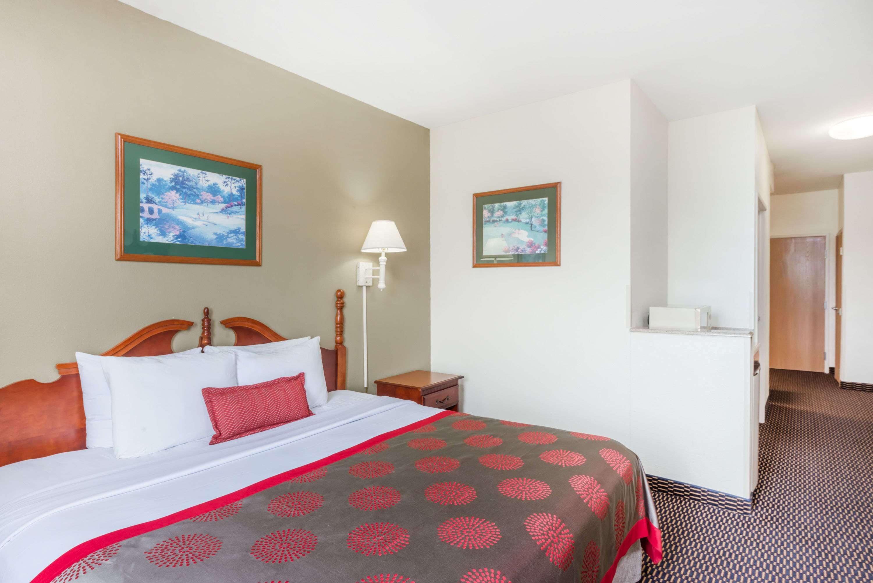 A hotel room with a bed, a nightstand, a lamp, and two framed pictures on the wall.