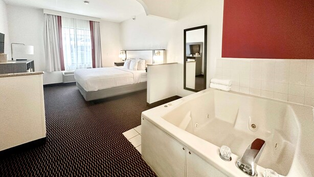 A hotel room with a large bed, a separate sitting area, a bathroom with a bathtub, and a large mirror. - Ramada by Wyndham Columbia (Columbia)