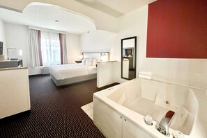 A hotel room with a large bed, a separate sitting area, a bathroom with a bathtub, and a large mirror. - Ramada by Wyndham Columbia (Columbia)