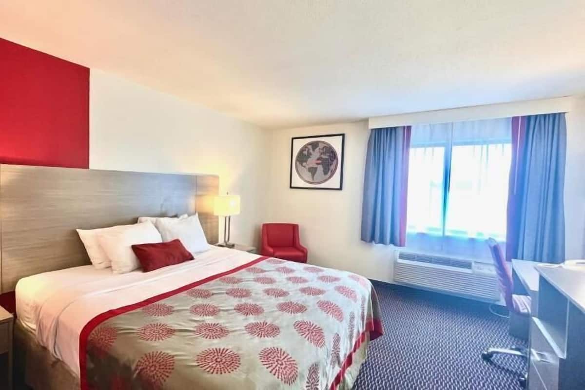 A hotel room with a bed, bedside lamps, a desk, and a window with curtains.