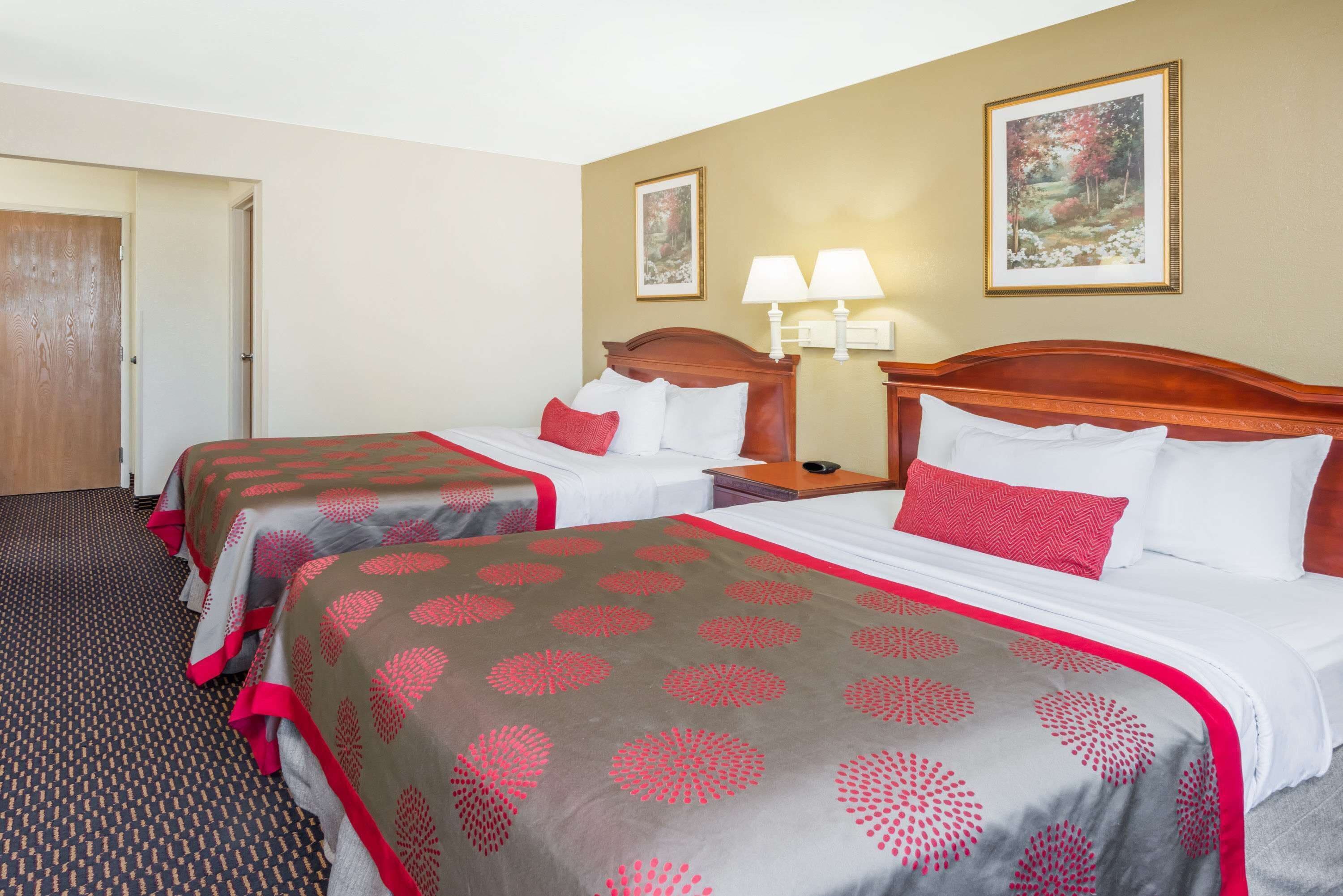 Une chambre d’hôtel avec deux lits, chacun recouvert d’une couvre-lit à motifs rouges et gris, doté d’une tête de lit en bois et agrémenté d’une table de chevet avec une lampe.