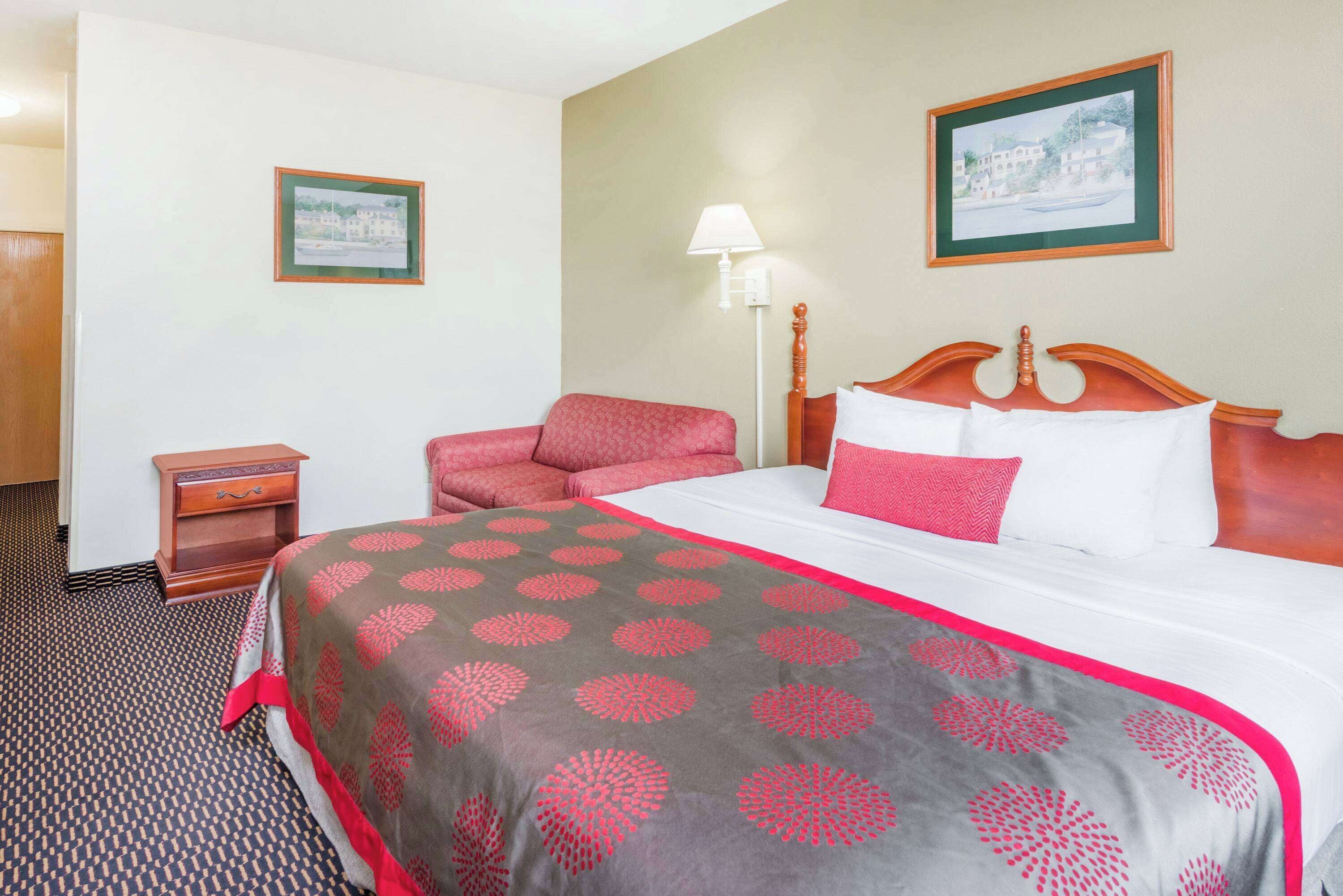 A hotel room with a bed, a chair, a nightstand, and a lamp.