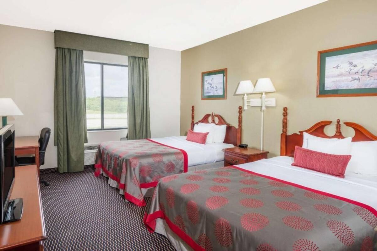 A hotel room with two beds, a desk, a chair, a TV, and a window with curtains.
