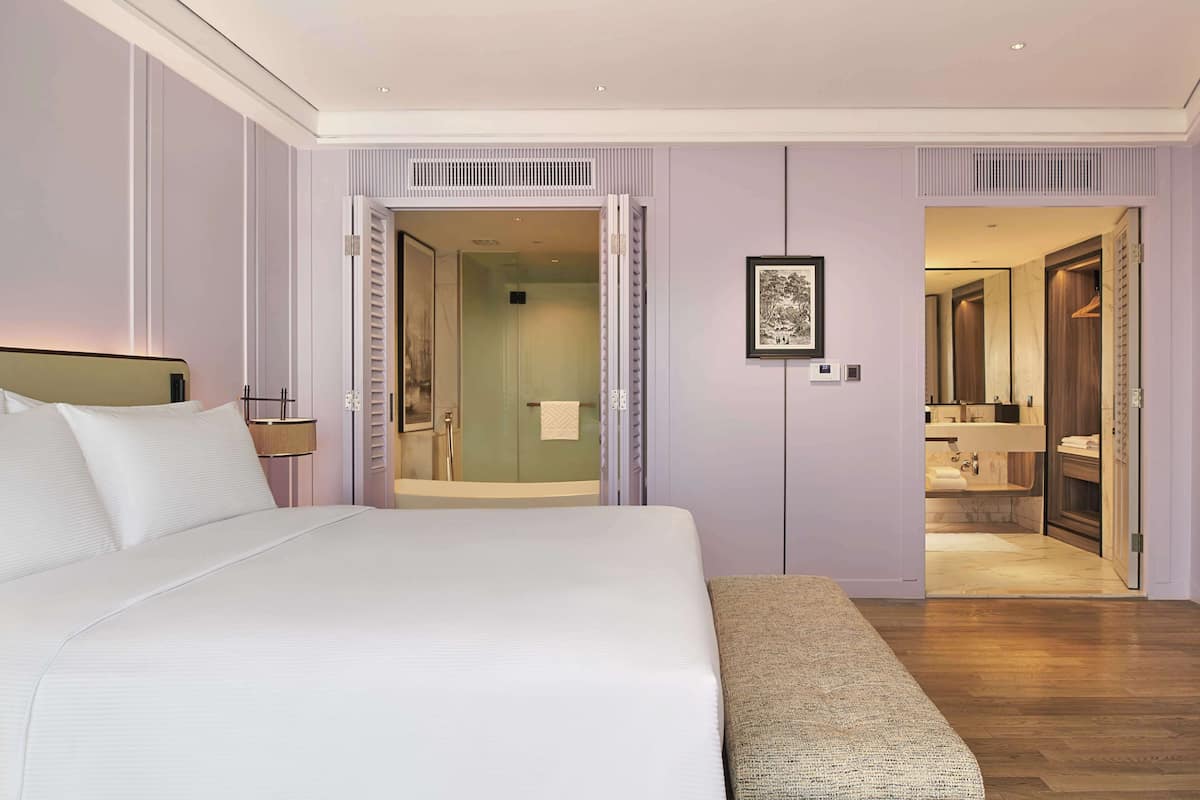 A hotel room with a large bed, a sitting area, a bathroom with a shower, and a mirror.