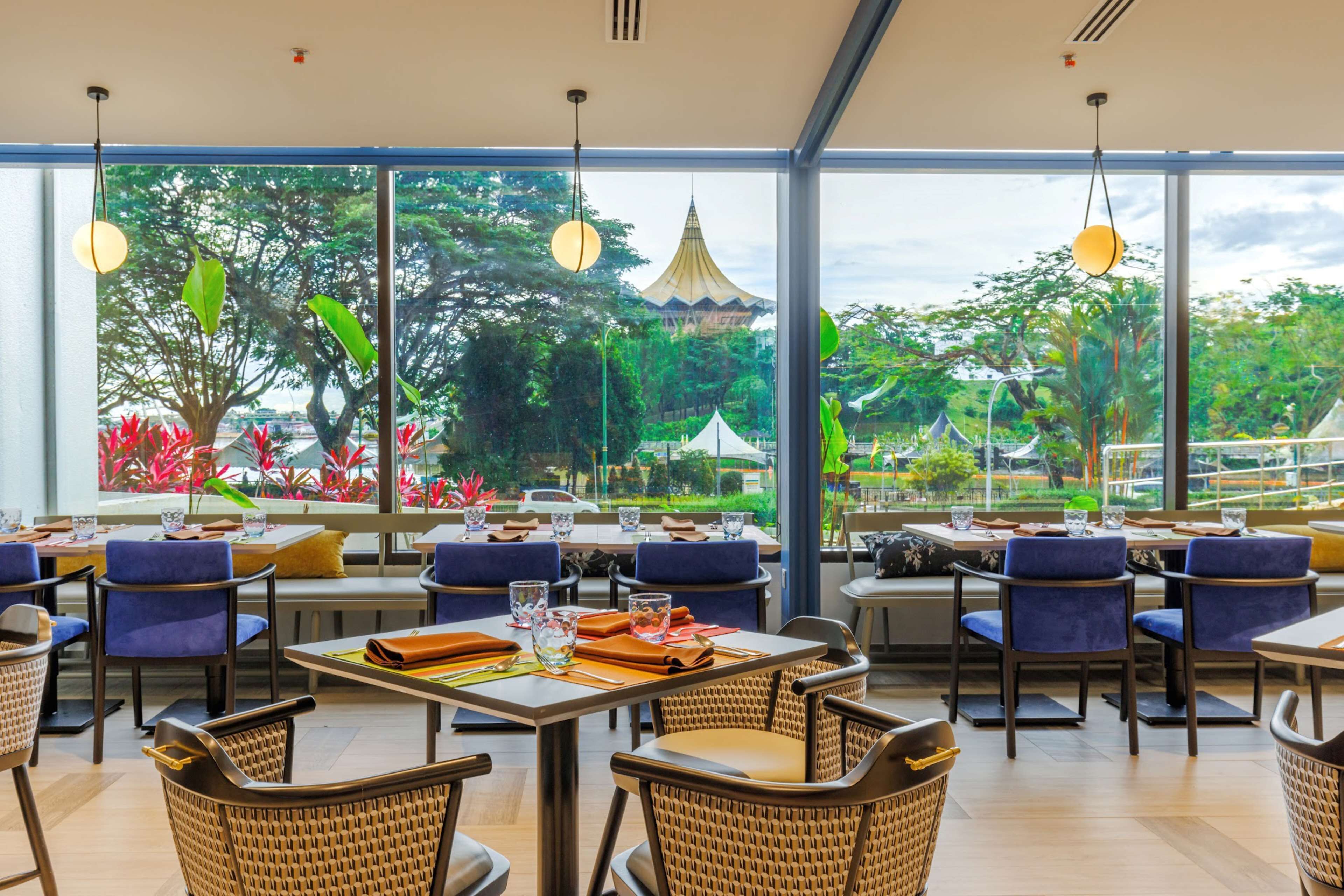 A restaurant with tables and chairs, large windows, and hanging lights.