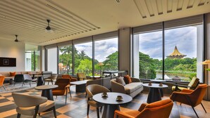 A modern lounge area with a checkered floor, comfortable seating, and large windows offering a view of a pagoda and lush greenery. - Hilton Kuching (Kuching)