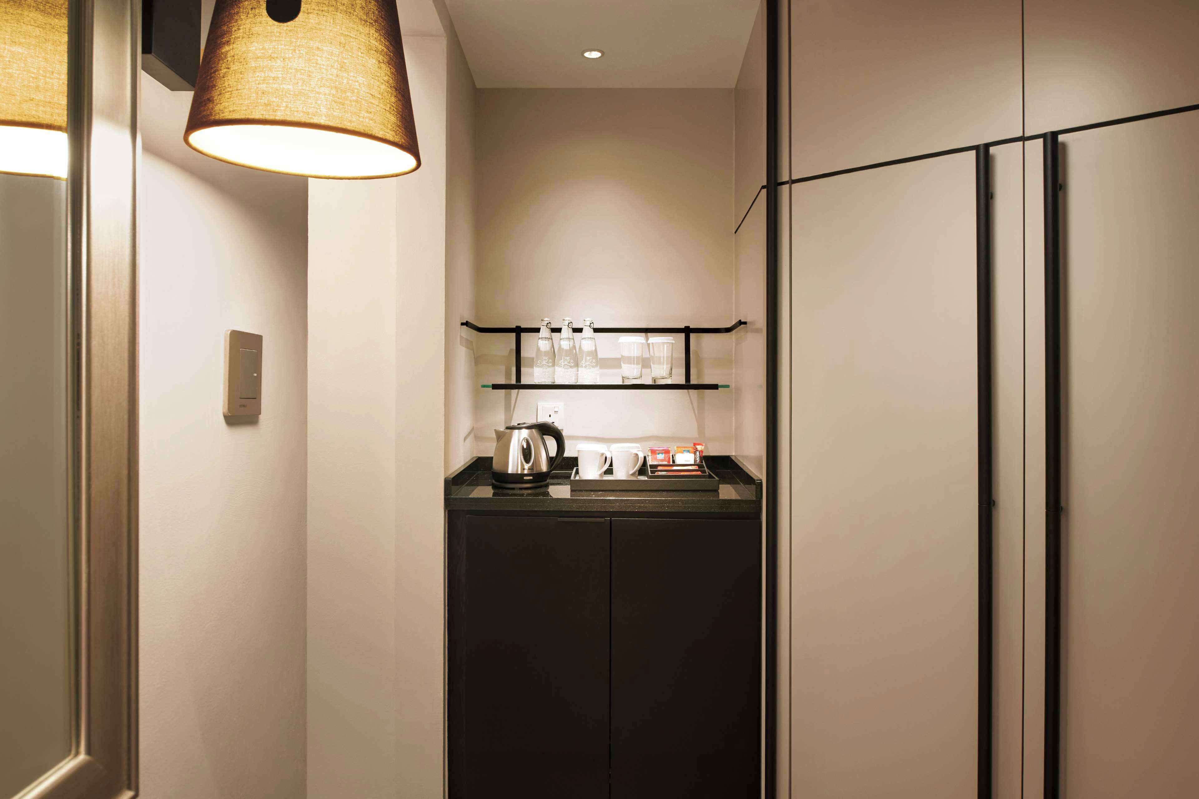 A compact kitchenette with a coffee maker, a kettle, and a shelf with glassware and a box of tissues.