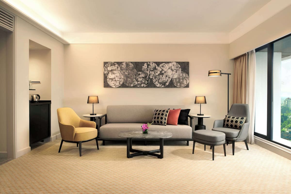 A modern hotel room with a sofa, two armchairs, a coffee table, and a large abstract painting on the wall.