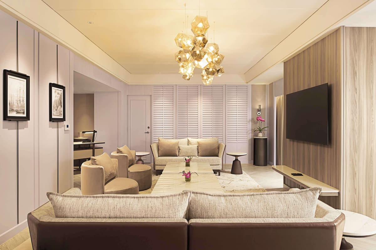 A modern living room with a central seating area, a chandelier, and a flat-screen TV mounted on the wall.