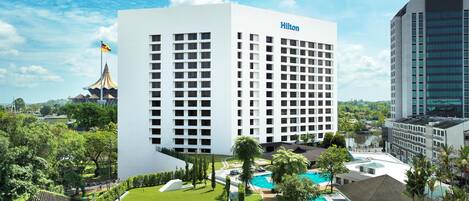 A Hilton hotel with a swimming pool, lush greenery, and a clear blue sky.