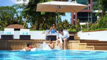 A swimming pool with lounge chairs and an umbrella, surrounded by greenery and a building.