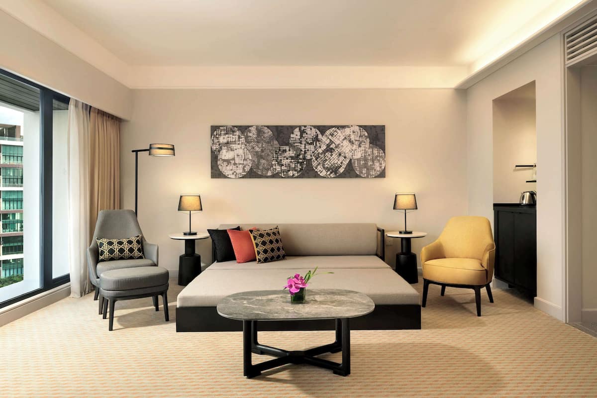 A hotel room with a sofa, two armchairs, a coffee table, and a large abstract painting on the wall.