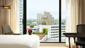 A hotel room with a large window offering a city view, a bed, a chair, and a small table. - Hilton Kuching (Kuching)
